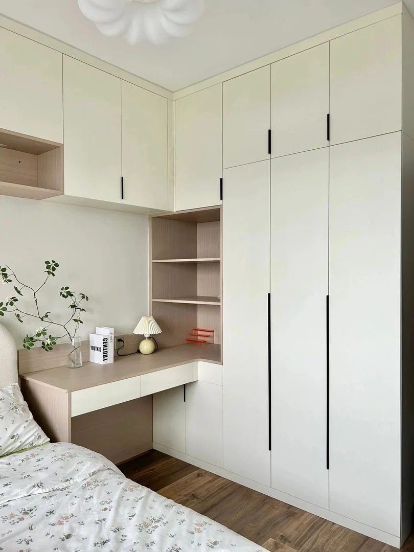Cream corner wardrobe with an integrated wood-look study desk beside a bed in a Singapore HDB bedroom