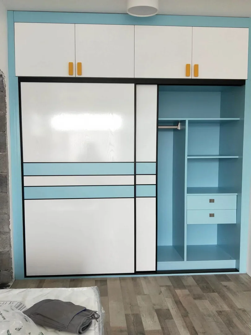 Blue and white built-in sliding door wardrobe with one panel open to show hanging space, shelves and drawers in a Singapore HDB bedroom